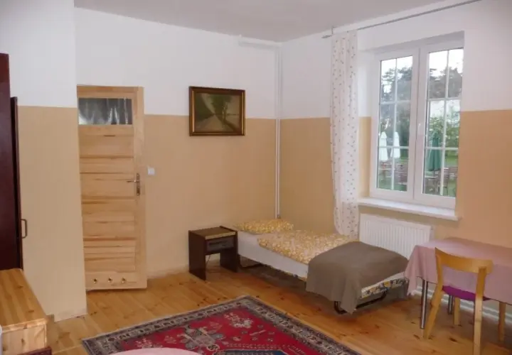 Pokój z łóżkiem, szafką nocną, drzwiami, oknem i dywanem.